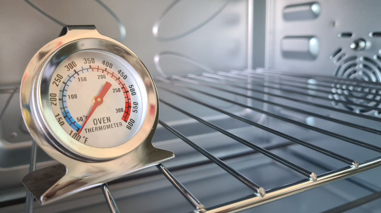 An analog oven thermometer resting on an oven rack in an empty oven