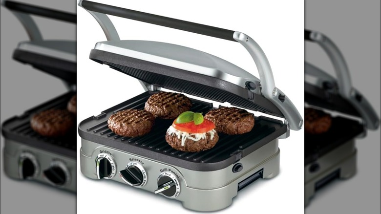 A panini press shows four burgers on the cooking surface.