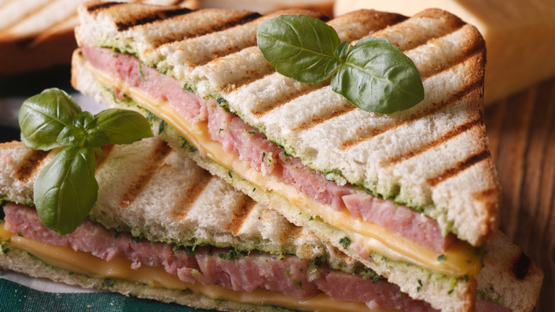 A sliced panini sandwich with ham, cheese, and pesto has a basil garnish.