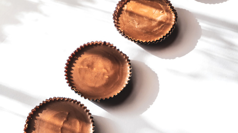 Three peanut butter cup candies in the sun on a white surface