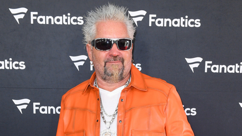 Guy Fieri wearing an orange jacket and sunglasses