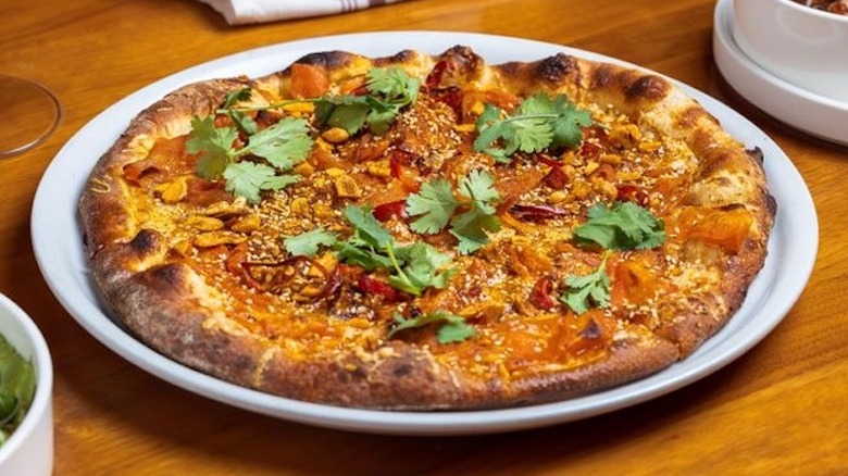 Whole Roasted Carrots pizza on round white plate, with parsley garnish, sitting on a wood tabe surrounded by a place setting