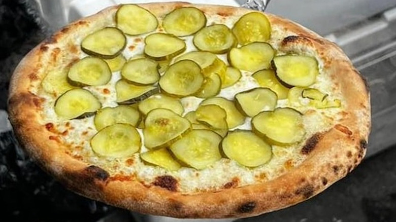 Whole white pizza with pickle slices on the top against an indistinguishable background