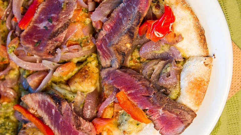 Rare steak, red onions, red peppers, on pizza crust, sitting on white plate