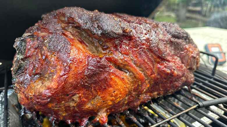 A portion of pork shoulder cooks on a grill outdoors.