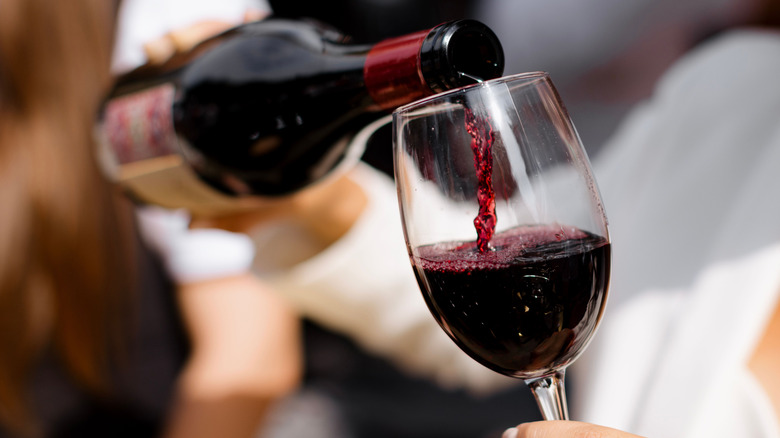 A hand pouring a bottle of red wine into a glass
