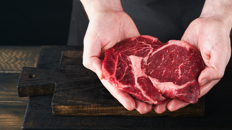 A chef holds a ribeye steak.