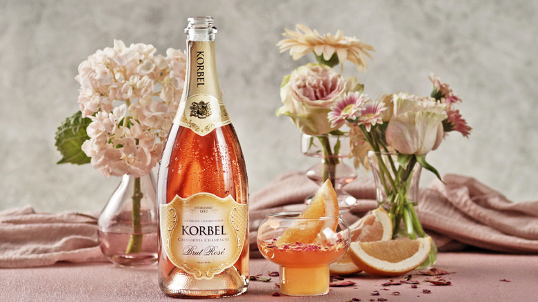 Bottle of Korbel Brut Rosé with a cocktail and several vases of pink flowers.