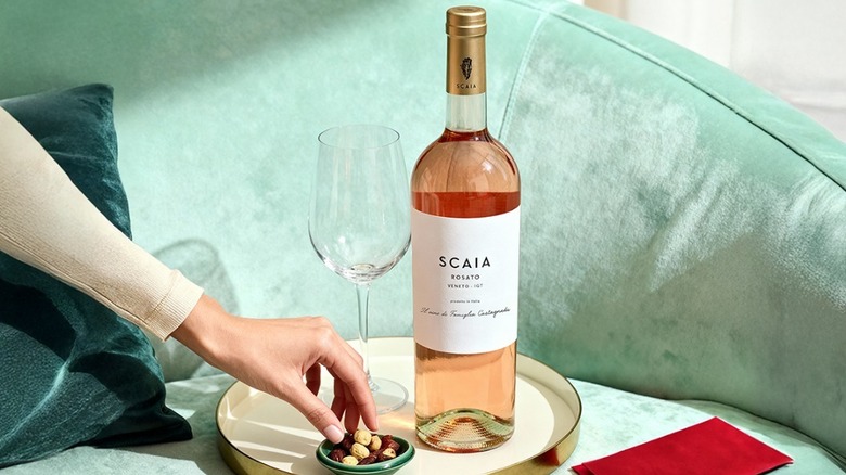 Bottle of SCAIA Rosato on a tray with a hand reaching for nuts from a dish.