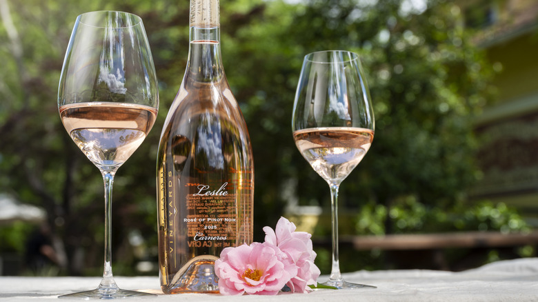 Bottle of Leslie Rosé between two glasses with some pink flowers.