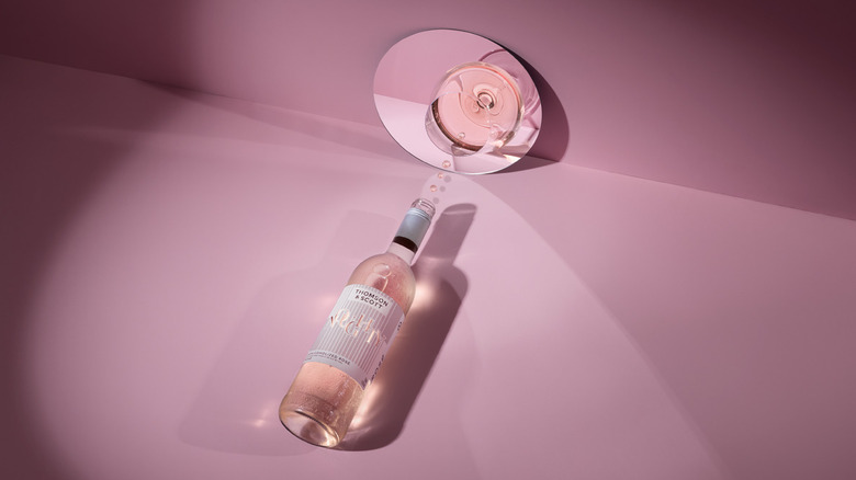 Artistically styled bottle of Noughty Rosé on a pink background with a glass of wine in a mirror.