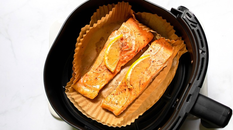 Two pieces of cooked salmon topped with lemon slices in a parchment-lined air fryer basket.