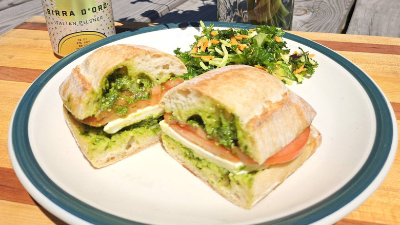 A pesto caprese and salad on a plate with a canned drink and plant in the back