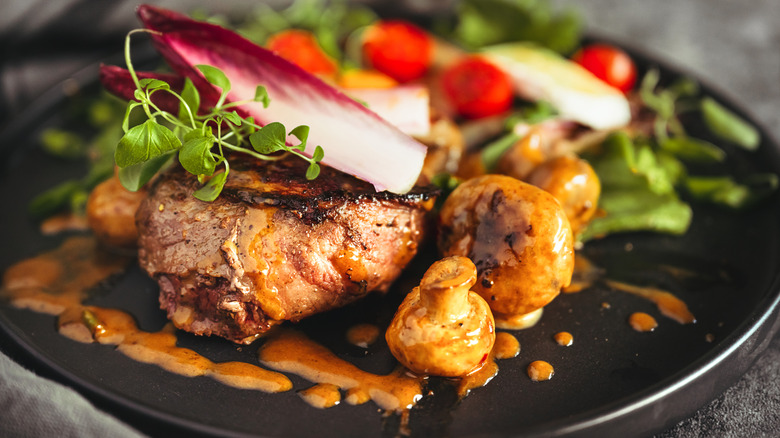 steak with bourbon cream sauce on black plate with salad