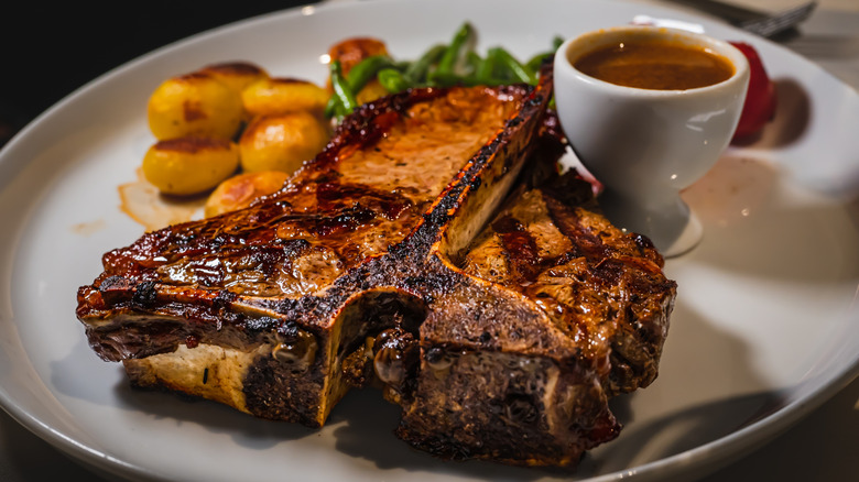 T-bone steak on white plate with steak sauce potatoes and string beans