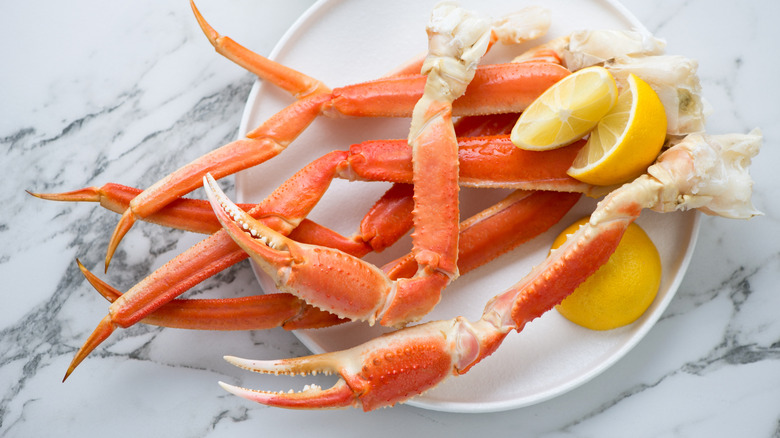 Plate of crab legs with lemon on white marble surface