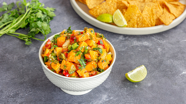 Mango salsa in a bowl with herbs and chips