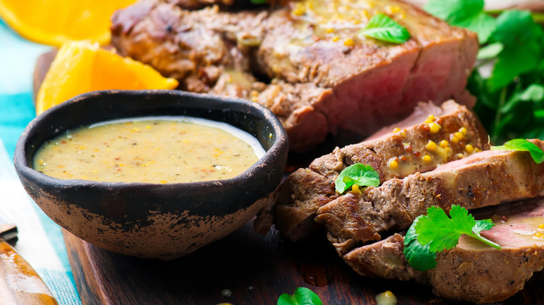 Pork next to a black bowl of creamy mustard sauce
