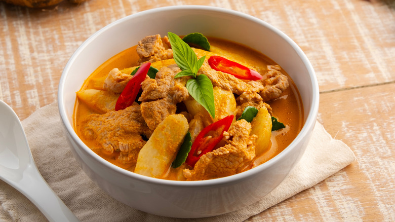 A white bowl of pork curry on a placemat