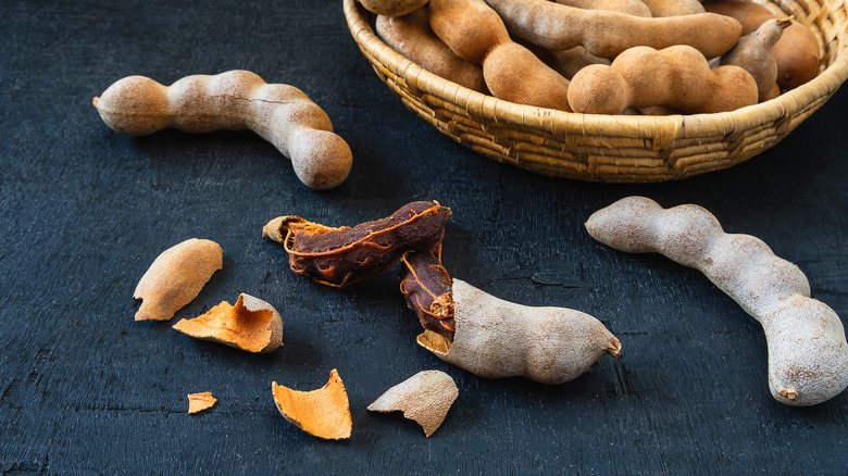 Tamarind fruit next to a bowl of tamarind on a black table