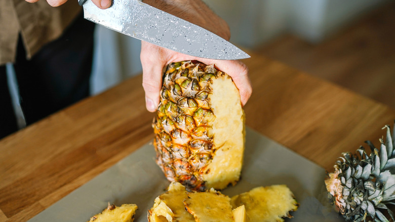 cutting a fresh pineapple on a cutting board