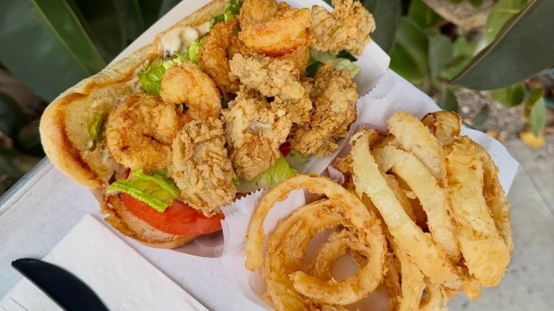 Shrimp po'boy and onion rings on plate outside