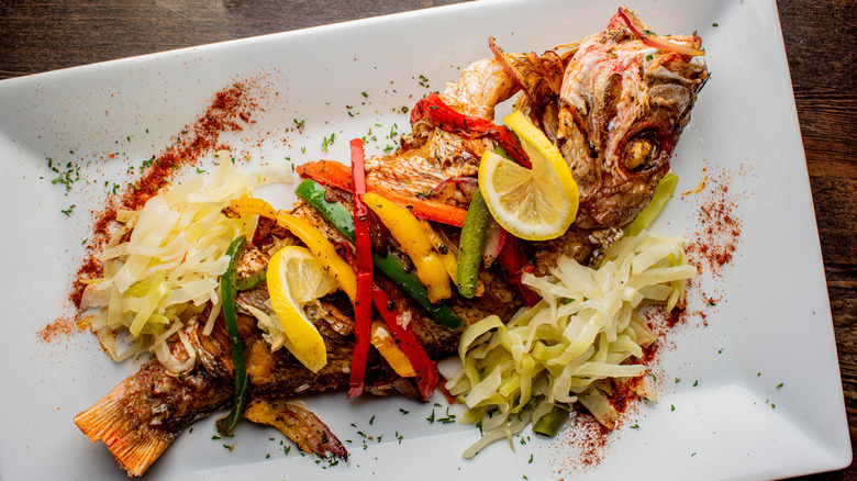 Whole red snapper on plate with lemon and veggies