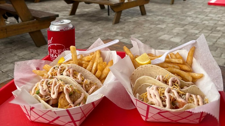 Fish tacos and fries on red tray in front of patio and picnic tables