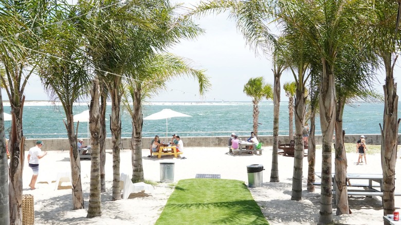 White sand beach with palm trees and people eating at tables with water in background