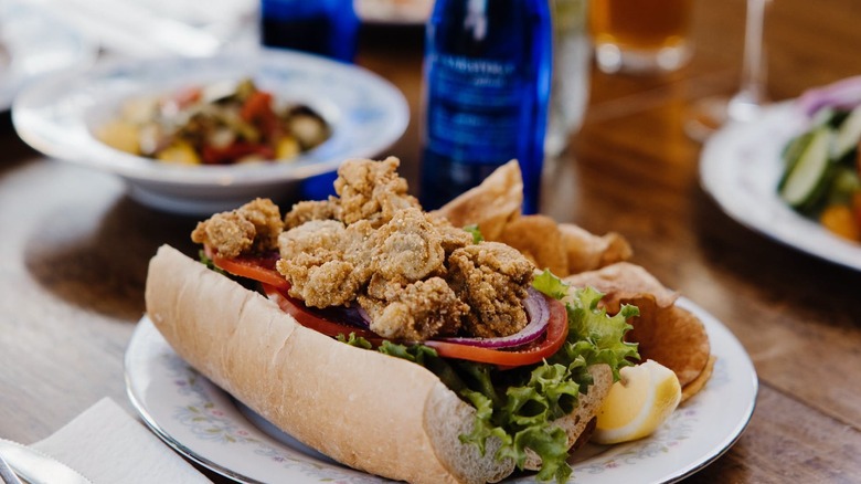 Shrimp po'boy on table outside with other dishes blurred in background