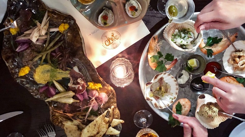 Platter with assorted seafood and oysters on table with drinks and candle
