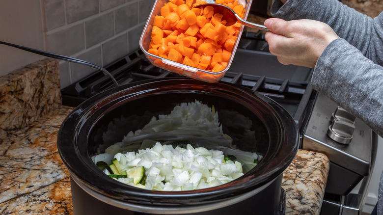 Hands adding raw ingredients to a slow cooker.
