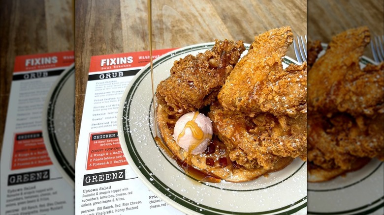 Honey being poured over a plate of chicken waffles with Fixin restaurant's menu on the side