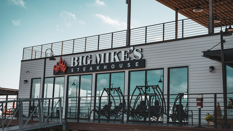An exterior of Big Mike's Steakhouse, showcasing its logo, with a few chairs out front and upstairs dining.