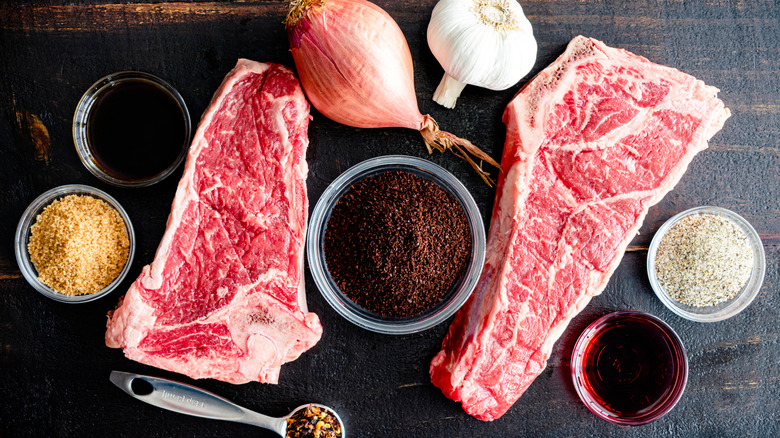 Two big, beautifully marbled steaks are surrounded by little bowls of standard seasonings, as well as ground coffee.