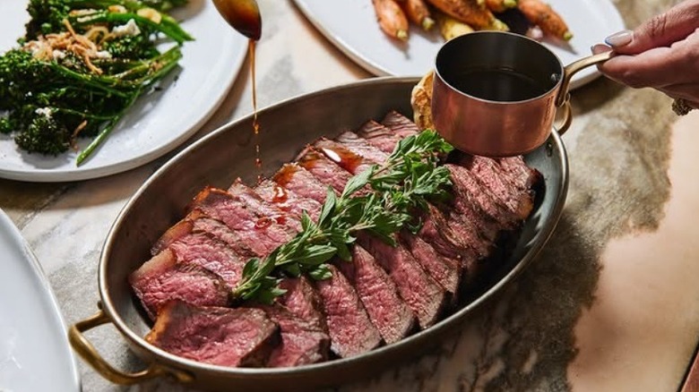 Hand drizzling sauce on steak at Gwen