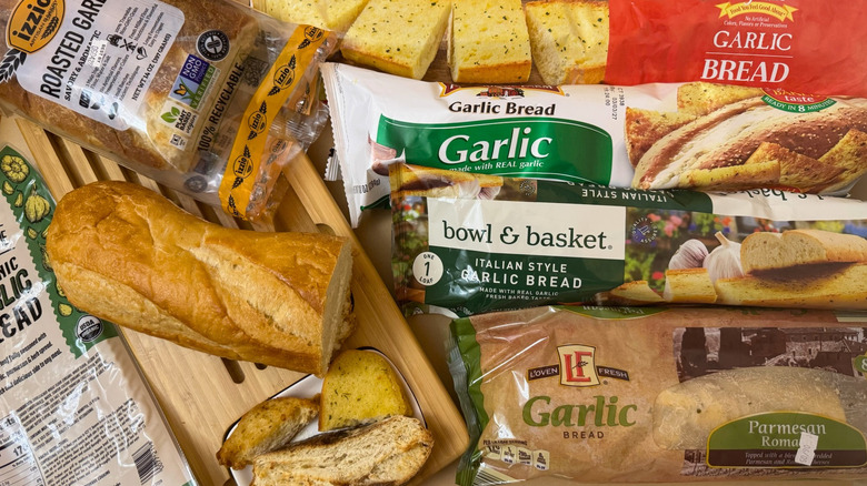 Loaf of garlic bread on wooden board surrounded by variety of packaged breads