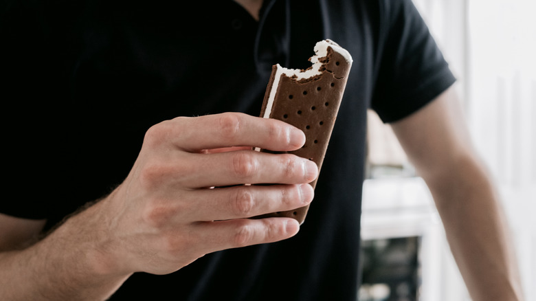 A person's hand is seen holding an ice cream sandwich with a bite taken out.