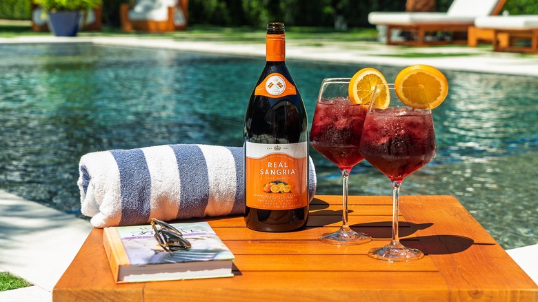 A bottle of Reál Sangria with two full glasses in front of a pool