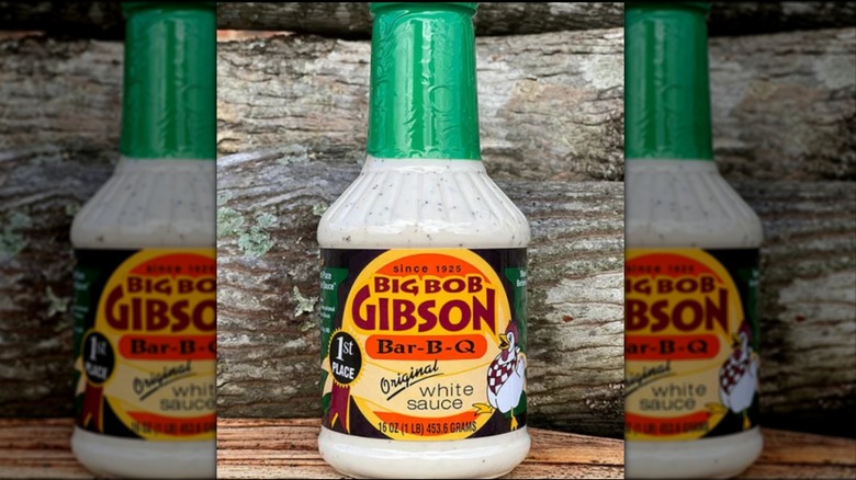 A bottle of Big Bob Gibson Original White Sauce on a wooden table with a log in the background