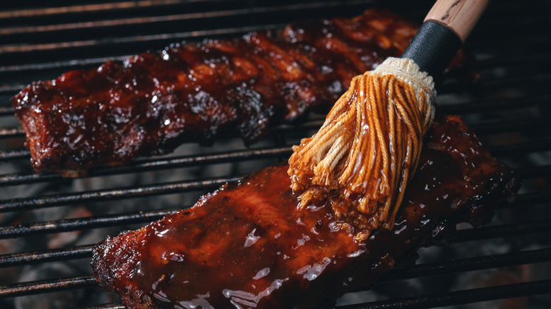 A close up picture of a brush glazing some ribs on the grill with sauce