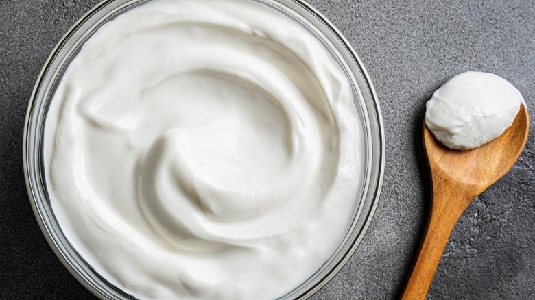 Sour cream in a clear glass bowl and on a skinny wooden spoon