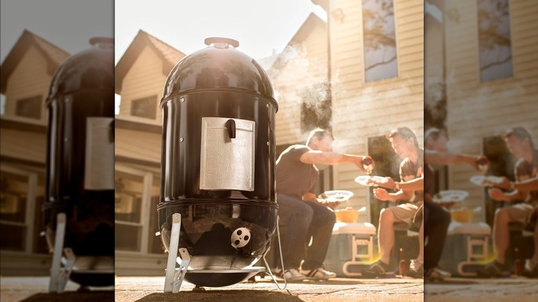 Weber smoker in use outdoors with two men in background