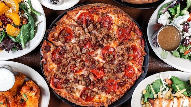 Candlelite Chicago tavern-style pizza cut in squares, loaded with meat, next to salads