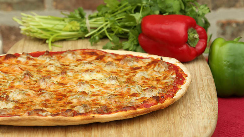 Frank's Pizzeria tavern-style pizza cut into squares on a wooden peel with peppers and herbs