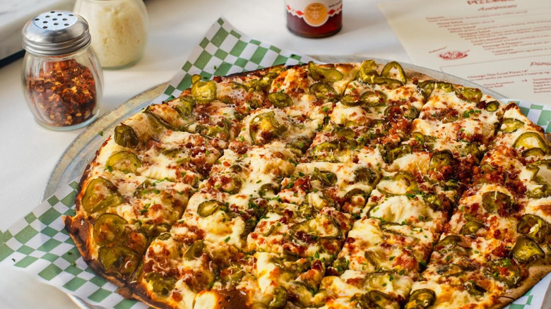 Pizz'amici thin crust pizza loaded with toppings on a green and white paper square on a table