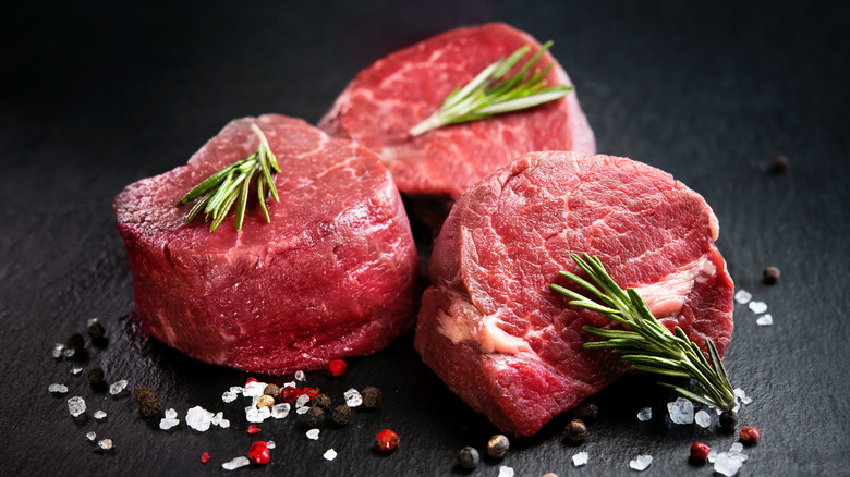 Three uncooked filet mignon steaks arranged with herbs and spices.