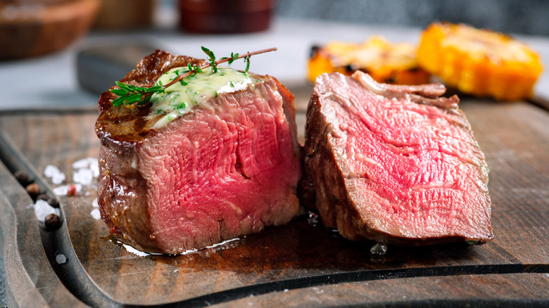 A medium rare filet mignon is halved to reveal its red interior.
