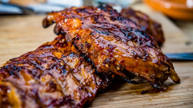 A rack of glazed ribs gleams on a wooden board