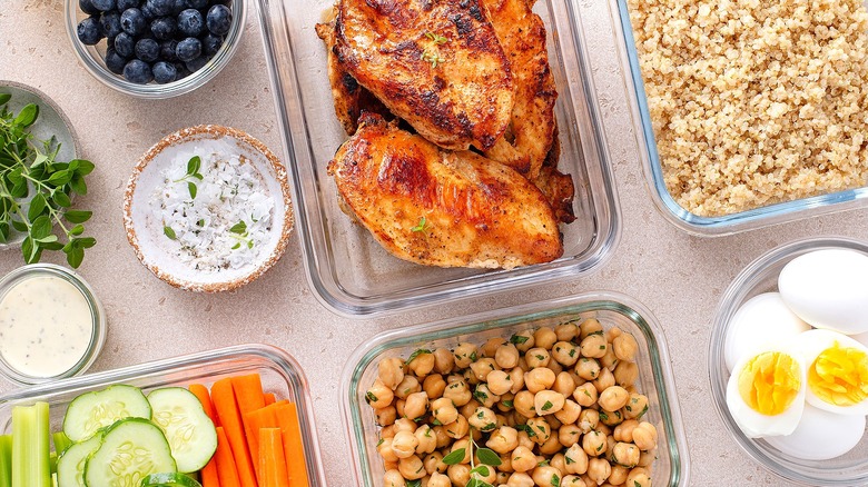 Seared chicken, raw chickpeas, sliced vegetables, and hard-boiled eggs in glass food containers.